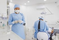 Жіночий стоматолог лікує зуби невпізнаваного пацієнта чоловічої статі проти колеги в уніформі в лікарні — стокове фото