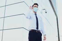 Знизу чоловічий підприємець у формальному носінні з медичною маскою, що дивиться далеко в місто під час пандемії коронавірусу — стокове фото