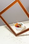 Высокий угол белая миска с вкусным блюдо тык и палочки для еды размещены за рамкой на столе покрыты кунжутом семян — стоковое фото