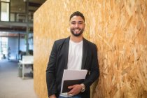 Delighted male entrepreneur with documents standing near wall in modern coworking space and looking at camera — Stock Photo