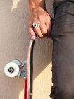 Crop anonymous male skateboarder in ring with skull standing with skateboard against wall in sunlight — Stock Photo