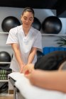 Щасливий масажист в білому халаті масажуючи теля жіночого пацієнта врожаю під час сеансу фізіотерапії в клініці — стокове фото