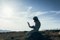 Ganzkörper-Astronaut im Raumanzug surft Daten auf Netbook, während er mit raketenförmigen Antennen auf einem Felsen außerhalb der Station sitzt — Stockfoto