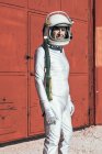Uomo in tuta spaziale in piedi vicino al muro rosso della struttura industriale nella giornata di sole — Foto stock