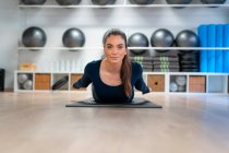 Full body of young female doing Locust pose while practicing yoga in studio looking at camera — Stock Photo