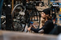 Side view of young skilled male mechanic with tool assembling chain wheel on bicycle during repair service works in workshop — Stock Photo