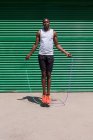 Сосредоточенные афроамериканский спортсмен скакалка во время кардио тренировки в солнечный день в городе — стоковое фото