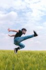 Вид збоку чоловік в джинсовому стрибку з піднятою ногою над високою травою в похмурому полі — стокове фото