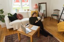 Высокий угол зрения женщины-радиоведущей, пишущей в тетрадке, сидя дома на полу и записывая подкаст — стоковое фото
