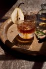 From above of elegant glass of cold whiskey decorated with pear slice served on tray with cigar in daylight — Stock Photo