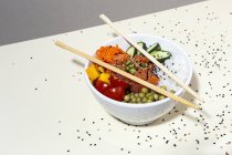 Dall'alto bacchette di bambù poste in cima alla ciotola con gustoso piatto di punta sul tavolo ricoperto di semi di sesamo — Foto stock