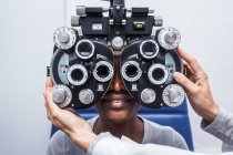 Optometrist adjusting the optometry equipment during study of the eyesight of a black woman — Stock Photo