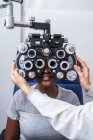 Optometrist adjusting the optometry equipment during study of the eyesight of a black woman — Stock Photo