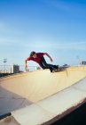 Maschio skateboarder equitazione skateboard sulla piattaforma sotto cielo blu nuvoloso in parco pattinaggio urbano nella giornata di sole — Foto stock