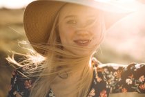 Retrato de una hermosa joven alegre con sombrero en el campo mirando a la cámara sonriendo - foto de stock