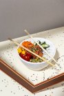 Angolo alto di ciotola bianca con gustoso piatto di punta e bacchette poste dietro telaio su tavolo ricoperto di semi di sesamo — Foto stock