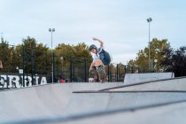 Teenage boy jumping with skateboard and showing stunt on ramp in skate park — Stock Photo