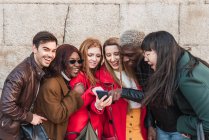 Empresa de amigos multiétnicos elegantes que se reúnem na rua e assistem vídeo engraçado no telefone celular juntos — Fotografia de Stock