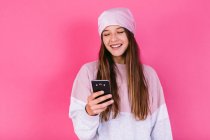 Adolescente femenina feliz con cabello castaño en pañuelo para la cabeza para el concepto de cáncer navegar por el teléfono celular - foto de stock