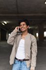 Jeune homme latino souriant en vêtements décontractés parlant au téléphone tout en se tenant debout dans le parking — Photo de stock