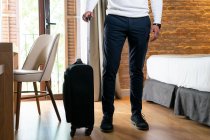 Hombre viajero con equipaje de pie cerca de la cama en la habitación de hotel - foto de stock