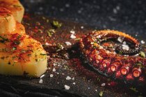 Von oben von gebratenem Tintenfisch-Tentakel und Kartoffelstücken serviert mit Gewürzen auf schwarzem Brett auf dem Tisch — Stockfoto