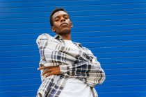 From below serious dreamy African American male standing looking at camera on background of blue wall in street — Stock Photo