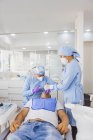 Stomatologue féminine traitant les dents d'un patient masculin méconnaissable contre un collègue en uniforme à l'hôpital — Photo de stock