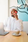 Счастливый мусульманский мужчина в подлинной одежде сидит за столом и просматривает нетбук в кафетерии — стоковое фото