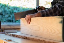 Crop falegname maschile irriconoscibile utilizzando sega affilata durante il taglio legname tavola al banco da lavoro in officina professionale — Foto stock
