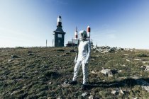 Ganzkörper-Mann im Raumanzug steht an sonnigen Tagen auf felsigem Boden gegen Metallzaun und gestreifte raketenförmige Antennen — Stockfoto