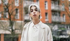 Mulher transexual auto-assegurada em roupas elegantes e com cabelos grisalhos olhando para a câmera na área urbana da cidade — Fotografia de Stock