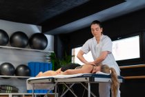 Дружня масажистка посміхається і масажує плечі жінки під час роботи в клініці фізіотерапії — стокове фото