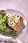 Alto ángulo de huevo frito en brioche servido en plato con lechuga fresca para un desayuno apetitoso sobre fondo rosa - foto de stock