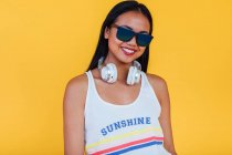 Entzückte Asiatin steht mit Sonnenbrille auf gelbem Hintergrund im Studio und blickt in die Kamera — Stockfoto