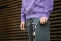 Cropped unrecognizable young male in casual clothes with skateboard looking at camera while standing near wall on street — Stock Photo