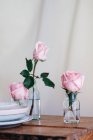 Рожеві троянди всередині скляних ваз, розміщені на дерев'яному столі на нейтральному фоні — стокове фото