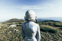 Vista posteriore astronauta maschio in tuta spaziale e casco in piedi su erba e pietre negli altopiani — Foto stock
