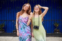 Young trendy female friends wearing summer dresses and sunglasses standing together in city street and looking at camera — Stock Photo