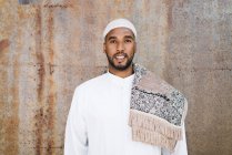 Islamic male in authentic white clothes while standing against grungy wall — Stock Photo