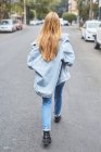 Back view of young female in sunglasses and denim clothes laughing in street while enjoying weekend and looking at camera — Stock Photo