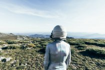 Back view male astronaut in spacesuit and helmet standing on grass and stones in highlands — Stock Photo