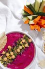 Draufsicht auf appetitanregenden Rote-Bete-Hummus garniert mit Kichererbsen auf Stoffhintergrund mit Brot und frischen Karotten- und Gurkenstäbchen — Stockfoto