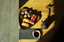 De arriba plato con surtidos rollos de sushi servidos sobre mesa con palillos y salsa de soja en restaurante japonés - foto de stock