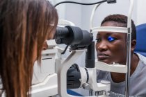 Optometrista ajustando o retinógrafo durante o estudo da visão de uma mulher negra — Fotografia de Stock