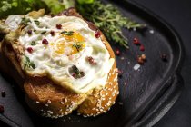 Смажене яйце на бріосі подається на підносі зі свіжим салатом для апетитного сніданку на чорному фоні — стокове фото