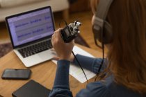 Вид збоку обрізаної невпізнаваної жінки в навушниках, що записують подкаст під час розмови в мікрофоні та використання ноутбука вдома — стокове фото