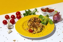 Köstliche Omelette mit gehackter Petersilie auf Teller gegen sonnengetrocknete Tomaten und rohe rote Zwiebel auf zweifarbigem Hintergrund — Stockfoto