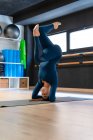 Corps complet de femme en forme dans les vêtements de sport faisant soutenu la posture de variation de la tête tout en pratiquant le yoga dans le studio de fitness — Photo de stock