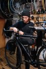 Serious male mechanic fixing handlebar of bicycle while working in repair service workshop — Stock Photo